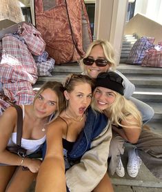 four women sitting on the steps posing for a photo with luggage in the back ground