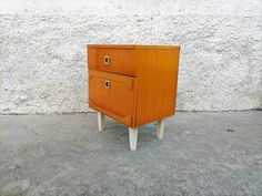 a small wooden cabinet sitting on top of a cement floor next to a white wall