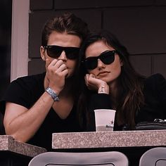 a man and woman sitting at a table in front of a window with their hands on their chins