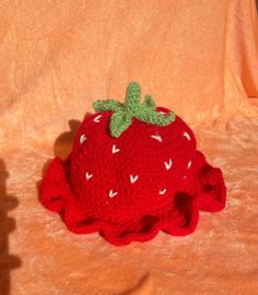 a crocheted strawberry hat sitting on top of an orange cloth covered bed sheet