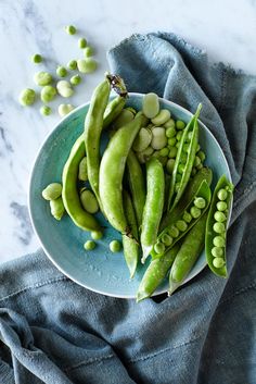 peas and pea pods in a bowl on a blue cloth next to some green beans