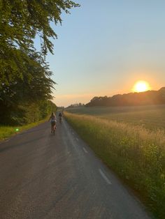 two bicyclists are riding down the road in front of the setting sun