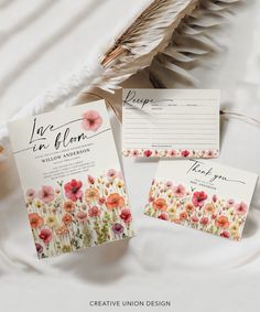 the wedding stationery is laid out on a bed with feathers, flowers and cards