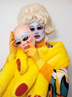 a woman in yellow holding a stuffed animal and another person with blue makeup on their face