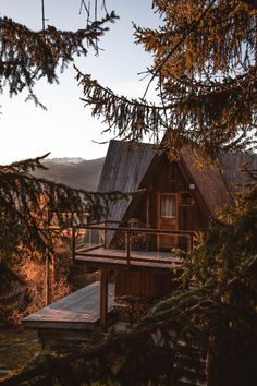 a wooden cabin nestled on top of a mountain with a deck and trees in the foreground