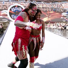two people dressed in red and gold dancing on a stage at a sporting event with fans watching from the bleachers