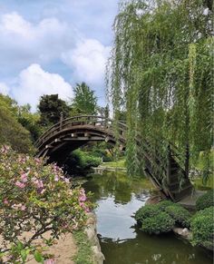 a wooden bridge over a small river in a park with trees and flowers on both sides