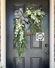 a wreath with white flowers and greenery hangs on the front door