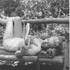 a woman laying on top of a wooden bench