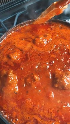 meatballs and sauce cooking in a pan on an open stove top with tongs