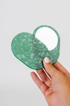 a hand holding an oval mirror in the shape of a heart on a white background