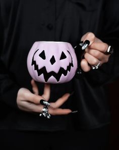 a woman holding a pink pumpkin shaped cup with black nail polishes on it's hands
