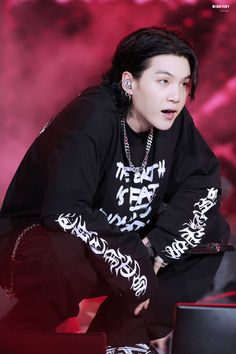 a young man with black hair and piercings sitting on a red background wearing a black hoodie