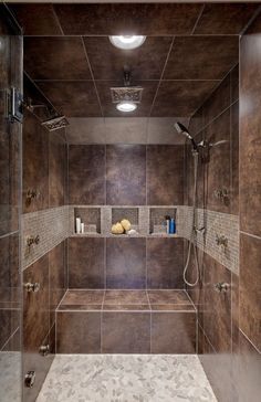 a walk in shower sitting next to a tiled wall and floor with brown tiles on the walls