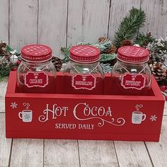 four jars with hot cocoa on them sitting in a red box next to pine cones