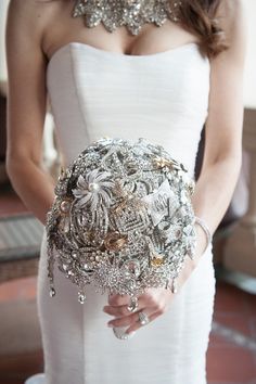 a woman in a white wedding dress holding a bridal bouquet with jewels on it