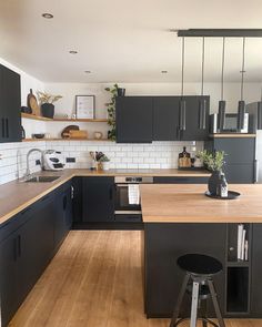 a kitchen with wooden floors and black cabinets, an island countertop and bar stools