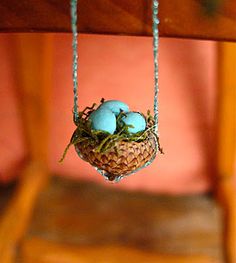 a bird's nest hanging from a chair with three blue eggs in the nest