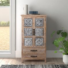 a wooden cabinet sitting next to a potted plant on top of a rug in front of a window