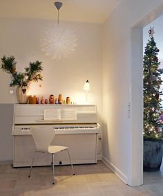 a white piano sitting in the middle of a living room next to a christmas tree