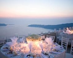 the table is set with white linens and place settings for dinner overlooking the ocean