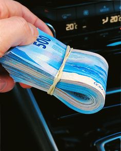 a person holding money in their hand while driving a car with the dash light on