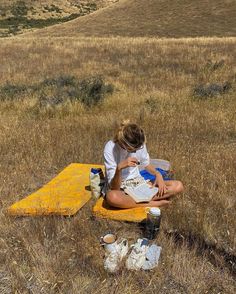 a woman sitting on top of a yellow blanket in a field next to a book