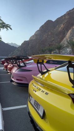 several different colored cars parked in a parking lot with mountains in the backgroud