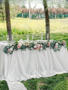 a table with flowers and wine glasses on it in the middle of a grassy field