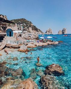 people are swimming in the clear blue water near some rocky coastlines and cliffs with boats