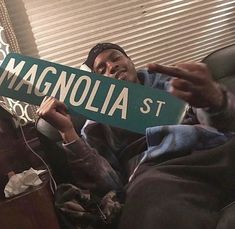 a man sitting on a couch holding up a green street sign that says magnolia st