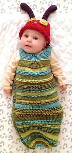 a baby laying on top of a bed wearing a knitted bug suit and hat