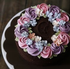 a chocolate cake with pink, purple and blue frosting on a white platter