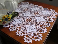 a white doily sitting on top of a wooden table next to a vase with flowers