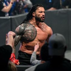 a man with long hair and tattoos on his arm standing in front of a crowd