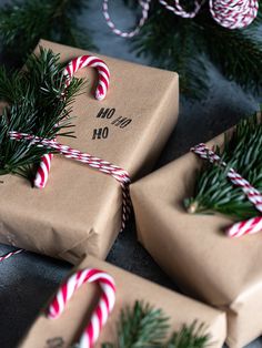 three wrapped presents with candy canes tied to them on a table next to christmas tree branches