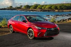 a red toyota camry parked on the side of the road near the water and trees