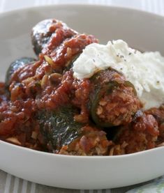 a white bowl filled with meat and veggies covered in sauce on top of a table