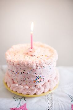 a pink birthday cake with sprinkles and a single candle