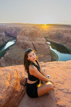 a beautiful woman sitting on top of a cliff next to a river in the desert