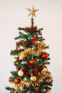 a small christmas tree with gold and red ornaments on it's top, against a white wall