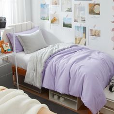 a bed with purple comforter and pillows in a bedroom next to a white wall