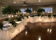 a banquet hall with tables covered in white cloths and decorated with greenery, candles and flowers