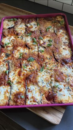 a square casserole dish with cheese and spinach toppings on a wooden cutting board