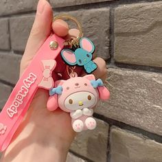 a hand holding a hello kitty keychain in front of a brick wall with an elephant on it