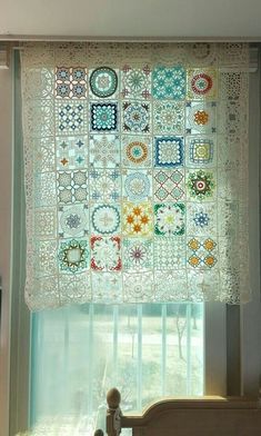 a bed sitting under a window next to a curtain covered in crocheted material