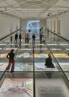 several people are standing in an art gallery looking at pictures on the walls and floor