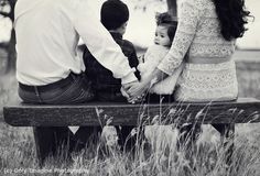 a family sitting on a park bench in the middle of an open field, holding hands and looking at each other