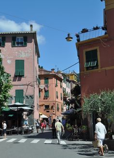 people are walking down the street in front of some buildings with green shutters and balconies