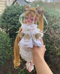 a hand holding a doll with blonde hair and white dress on it's head